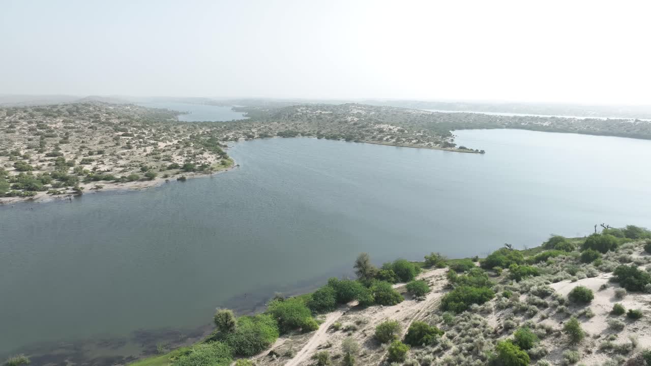 파키스탄 산하르의 보타르 호수의 드론 영화 촬영을 공개합니다. 아름다운 호수가 태양을 반사하고 섬으로 둘러싸여 있습니다.