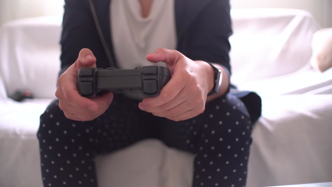Woman's hands using gamepad close-up view playing video console game at home sitting on the sofa