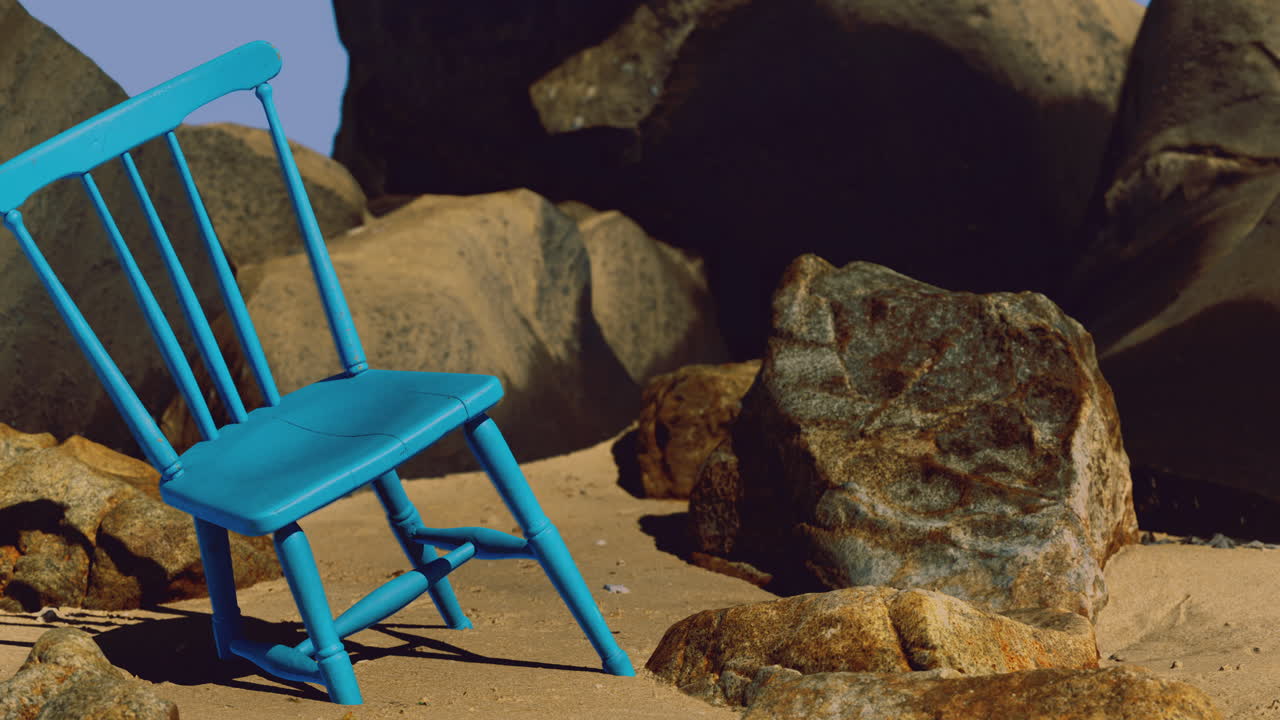 Bright blue chair placed among rocks on sandy beach under clear sky