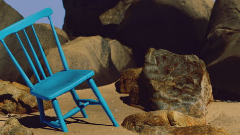 bright blue chair placed among rocks on sandy beach under clear sky