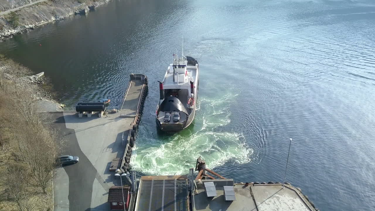 una foto de un avión no tripulado descendiendo de un ferry que se prepara para descargar coches en un muelle en un fiordo en noruega