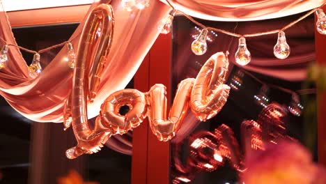 the word "love" made of pink balloons, with a backdrop of a light bulb garland, panorama