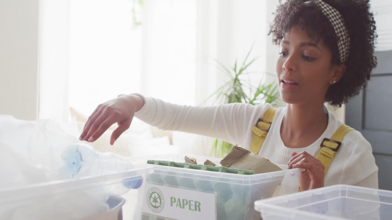 video de una mujer biracial feliz clasificando el reciclaje y sonriendo en casa, con espacio para copiar.