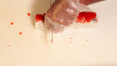 top view of a sushi roll being cut into pieces with a sharp knife - overhead shot, slow motion