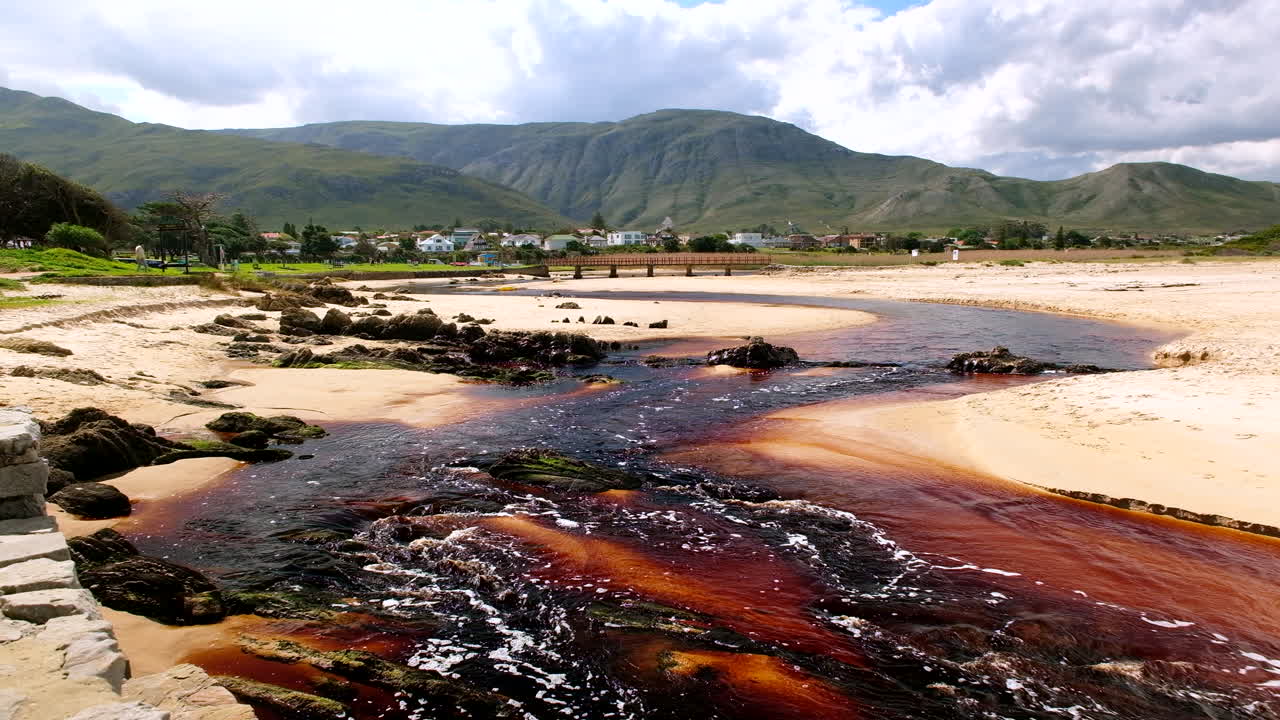 Brown tannin-rich Kleinmond lagoon water flows over beach toward ocean, scenic