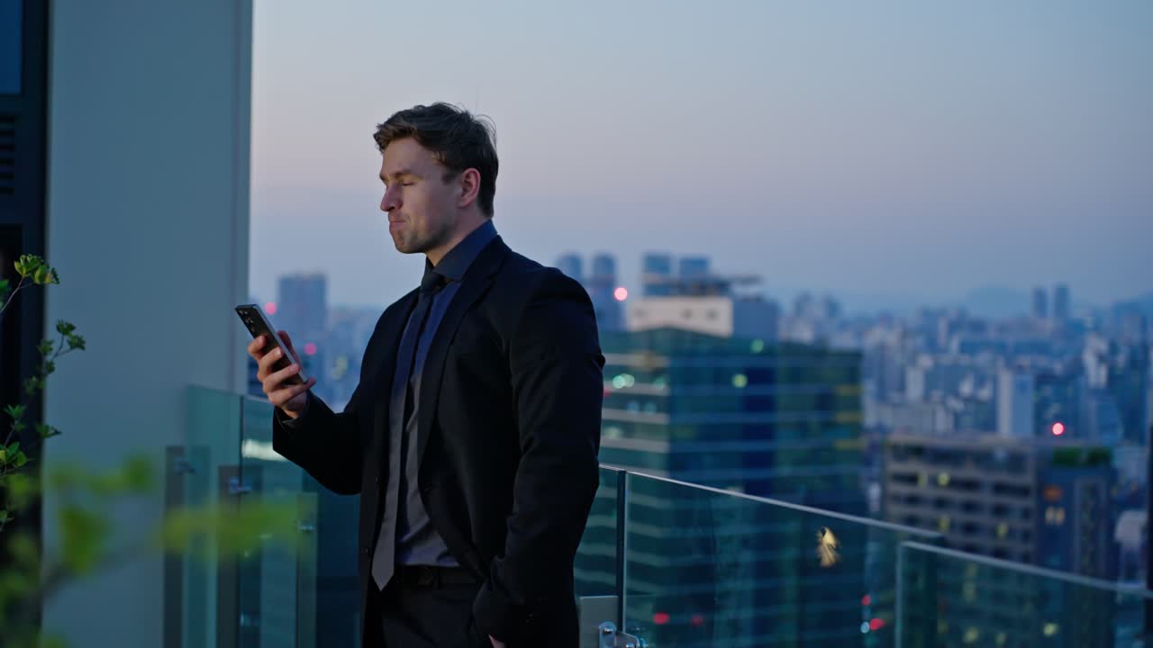 A businessman in a suit reads a message on his phone with disbelief and concern while standing on a rooftop at dusk, surrounded by a city skyline