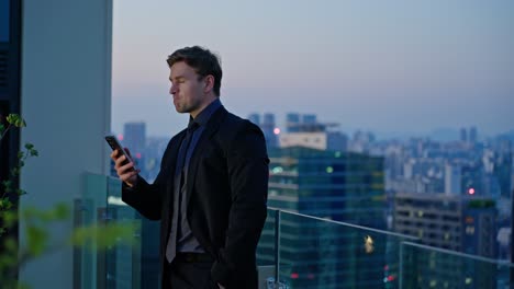 a businessman in a suit reads a message on his phone with disbelief and concern while standing on a rooftop at dusk, surrounded by a city skyline