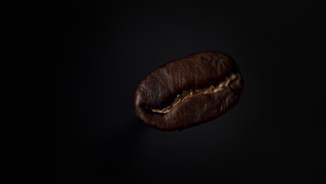 grano de café marrón oscuro girando en cámara lenta ante suelo negro con luz suave desde la izquierda