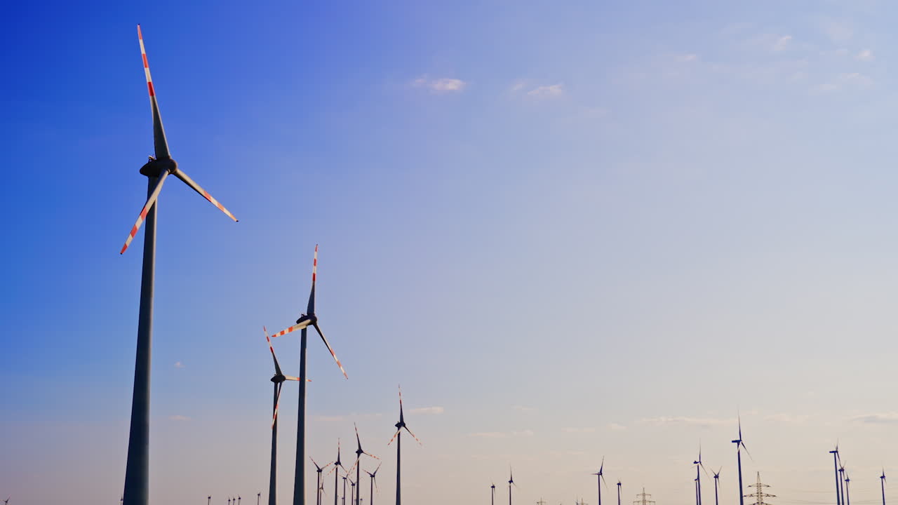 Wind turbines stand tall against the sky. Numerous wind turbines spin gently in a clear sky during a bright, sunny day, showcasing renewable energy in action