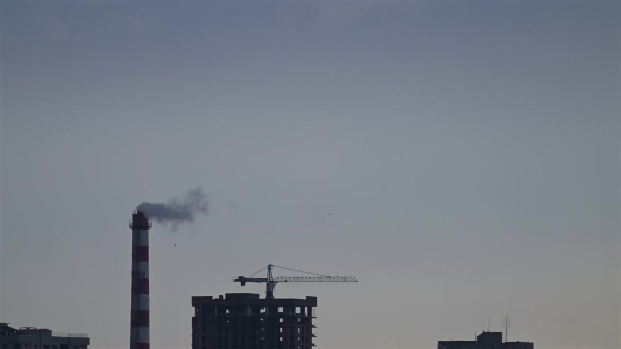 Time lapse of an industrial smokestack releasing emissions into the sky above a developing urban area