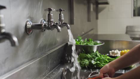 Caucasian-female-chef-washing-vegetables-in-colander-in-restaurant-kitchen