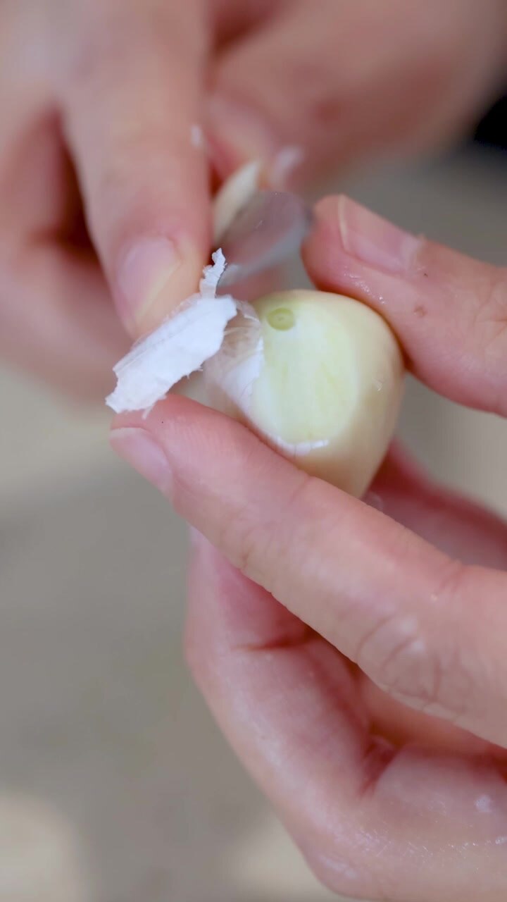 Hands skillfully peel garlic cloves on a light-colored countertop in bright, natural lighting