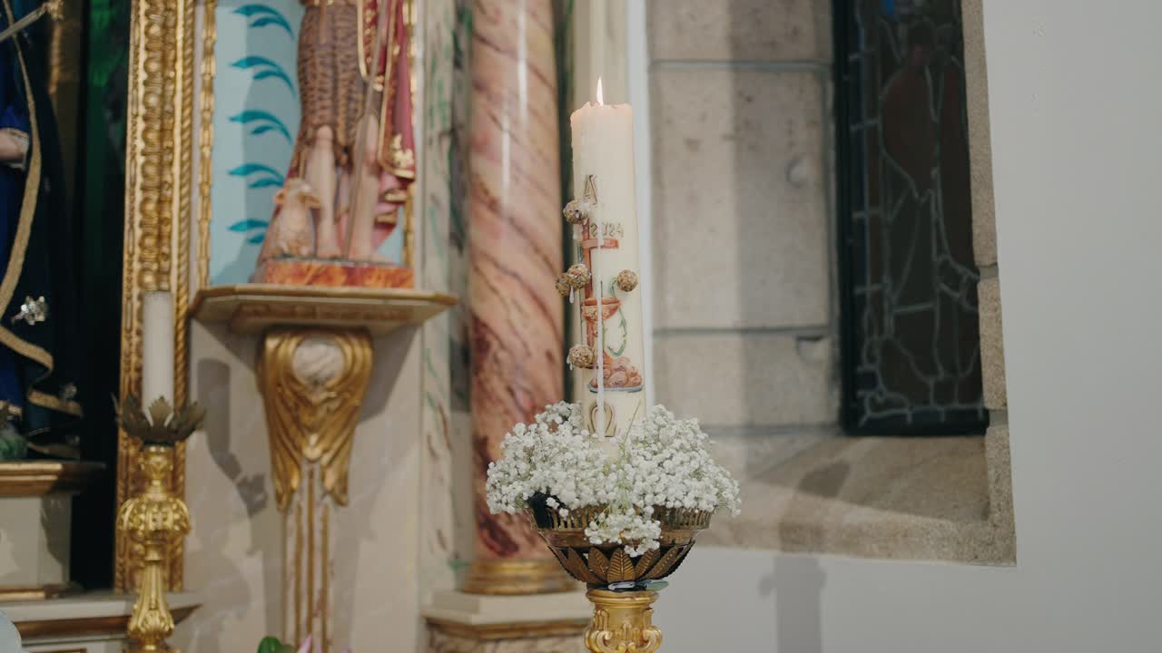 close up of a lit decorated candle with white flowers in an ornate church interior