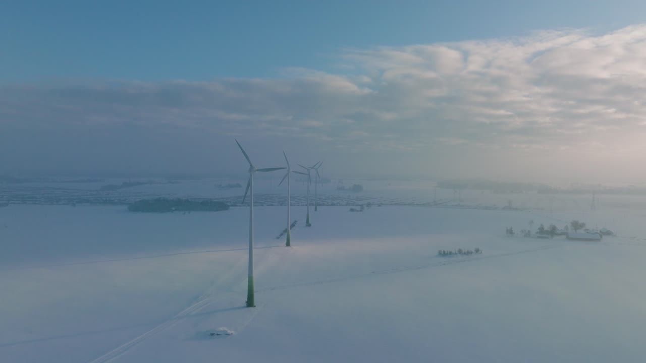 풍력 발전소에서 재생 가능한 에너지를 생성하는 풍력 터빈의 공중 전망, 안개로 가득 찬 눈으로 가득 찬 시골 풍경, 황금 시간 빛이 있는 화창한 겨울 저녁, 넓은 드론 샷