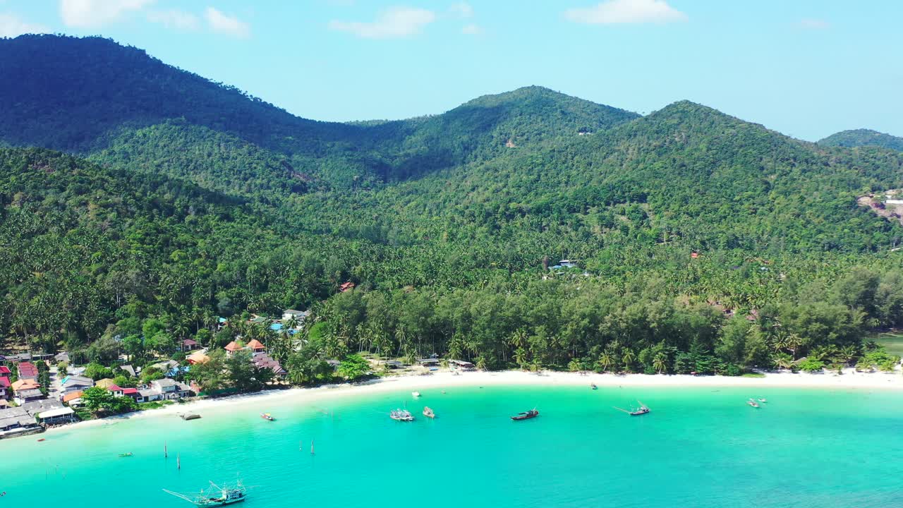 Aguas tranquilas y cristalinas de una laguna turquesa bañando una playa exótica virgen de arena blanca en una isla tropical con colinas verdes en Tailandia