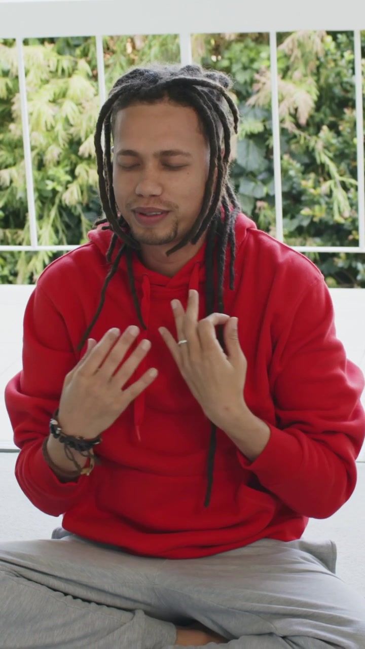 Vertical video: Reaching arms up, adult man in red hoodie stretching on balcony, centering breath