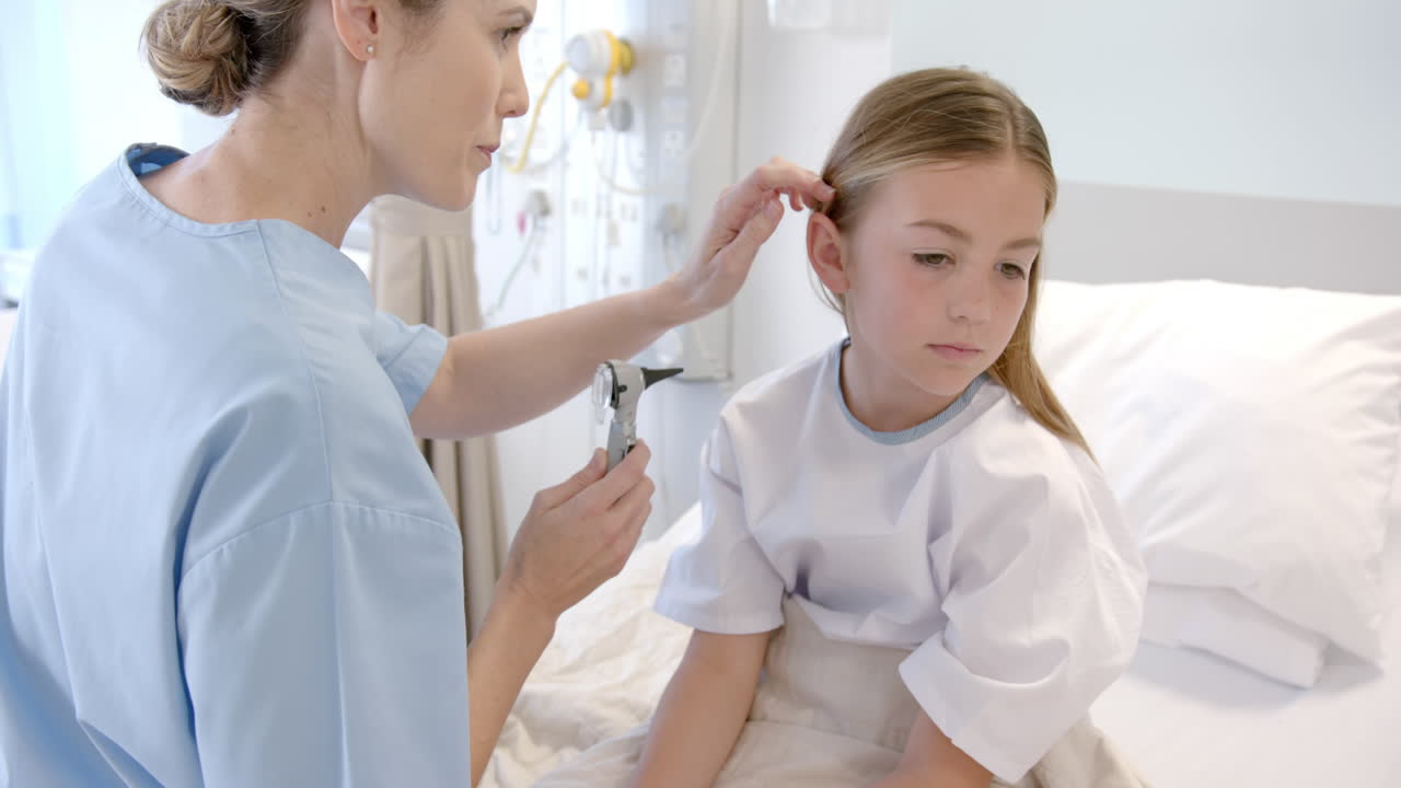 doctora caucásica usando un otoscopio para comprobar la oreja de una paciente en una cama de hospital, en cámara lenta