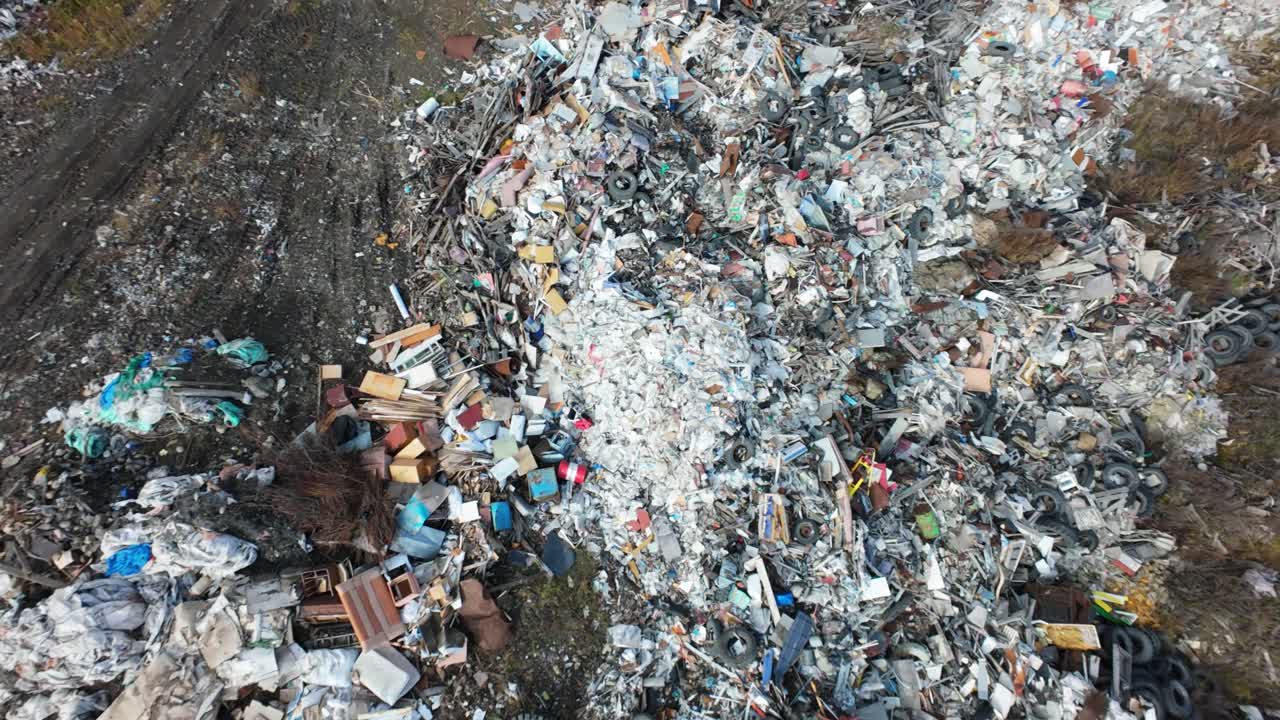 A close look at a household waste dump reveals a chaotic mix of discarded objects including furniture, plastics, and tires strewn across the site, highlighting the consequences of consumerism.