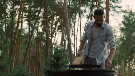 Focused-man-preparing-fire-for-bbq-outside.-Man-chef-putting-firewood-in-grid