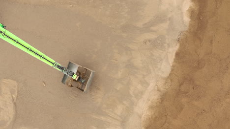 aerial view of a green arm operating in a sandy excavation site, moving sand with precision