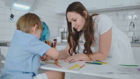 una hermosa madre y su hijo dibujan con lápices de colores sentados en la mesa en la cocina