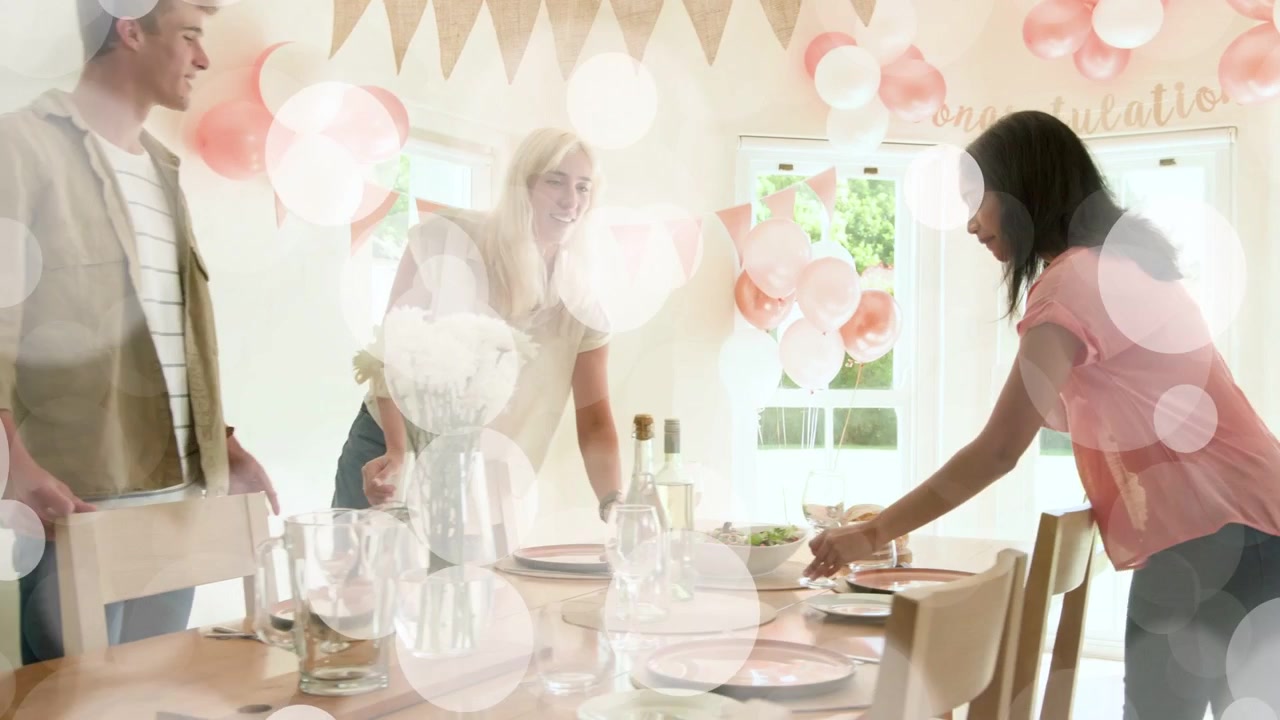 Förbereder sig för fest, tre vänner arrangerar tallrikar, vin, ballonger, kliver tillbaka för att överblicka bordet