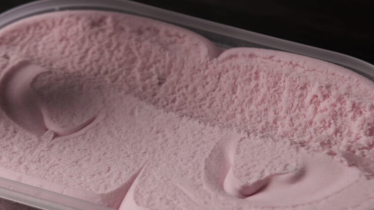 Close up view of a person scooping up fresh strawberry ice cream from tray.
