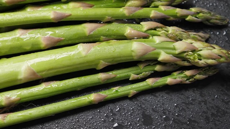 Raw green asparagus on wet black slate background. Rotating