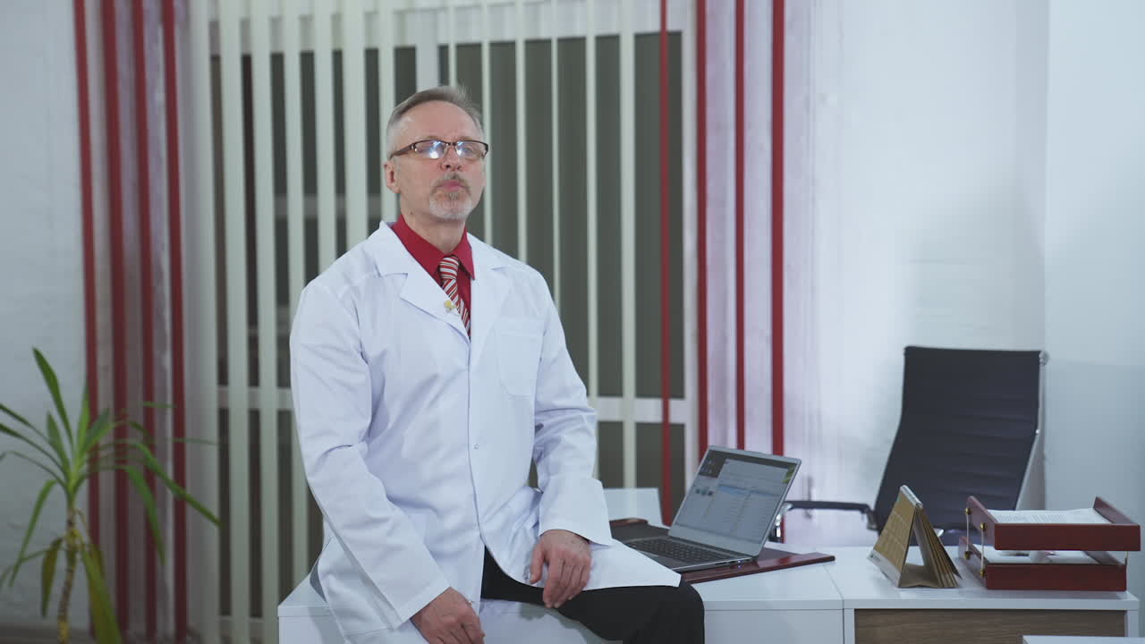 Medical consultation. Professional man doctor wears medical uniform talking on camera in the modern cabinet in clinic.