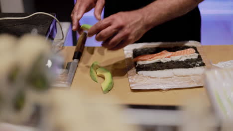 Detail-of-hands-preparing-a-sushi-roll-with-rice,-avocado-and-salmon