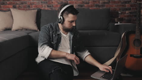 young musician man playing guitar, singing and using laptop at home