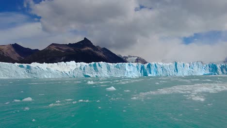 Astonishing-shot-of-Perito-Moreno-glacier-mixed-with-grey-clouds,-a-turquoise-lake-and-a-mountain