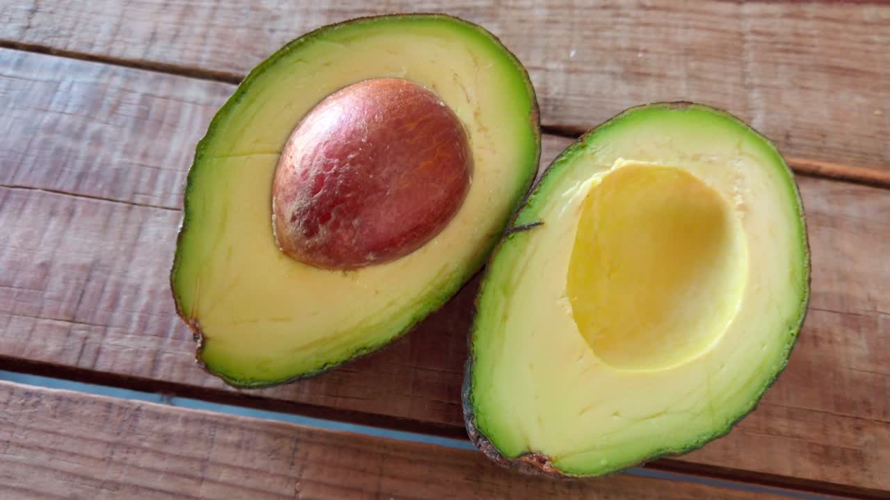Ripe avocado cut in half on a rustic wooden table, revealing green flesh and seed with a smooth semi orbit camera movement.