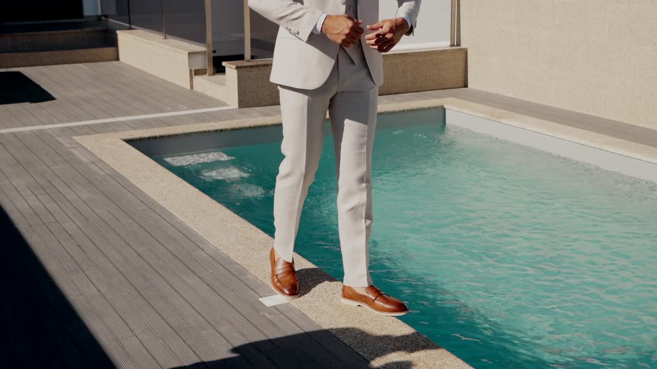hombre en traje formal caminando por una piscina moderna con cubierta de madera