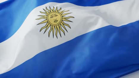 Pelota-De-Rugby-Blanca-Rodando-Sobre-La-Bandera-Ondeante-De-Argentina-Con-Espacio-Para-Copiar,-En-Cámara-Lenta