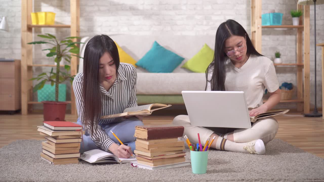 두 명의 귀여운 아시아 학생들이 거실에서 책과 노트북 에 바닥에 앉아 시험을 준비하고 있습니다.