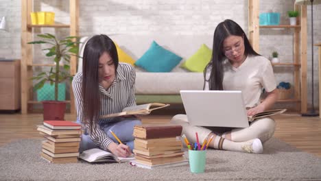 two cute asian students are preparing for the exam sitting on the floor next to books and a laptop in the living room