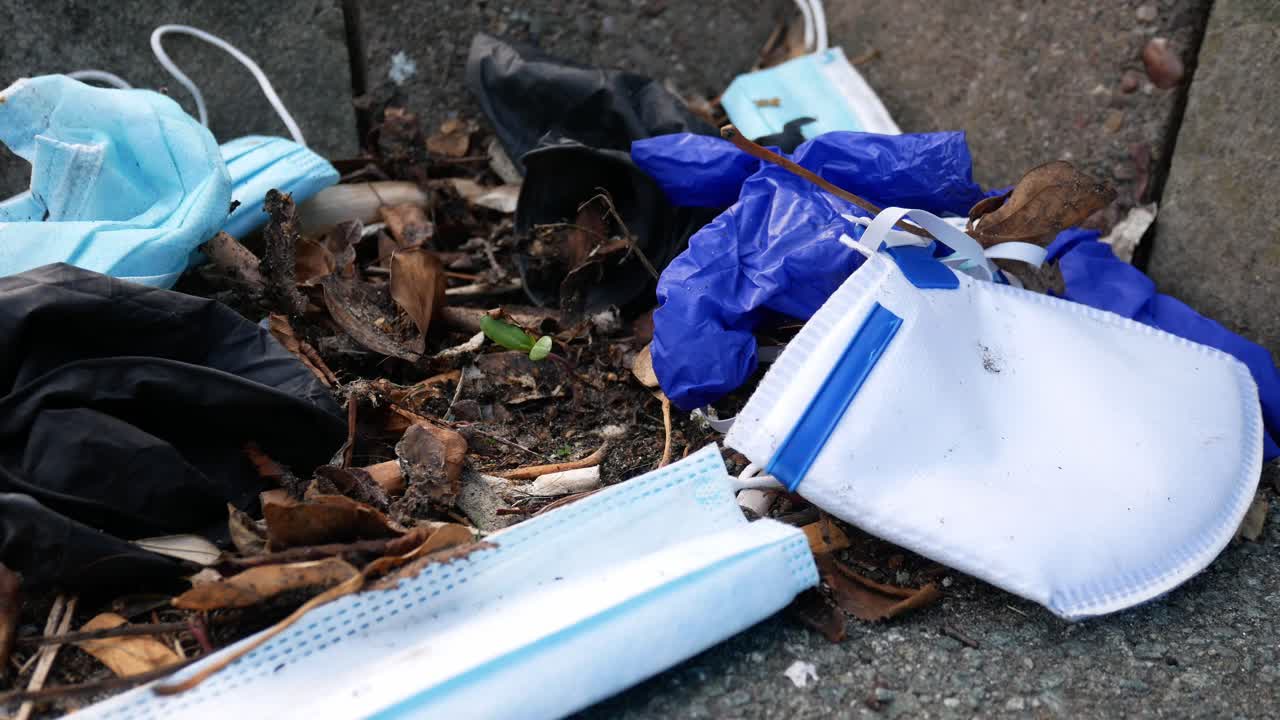 máscaras faciales desechables sucias para el virus de la corona y guantes de látex entre la basura de cigarrillos en el bordillo de la calle a la izquierda