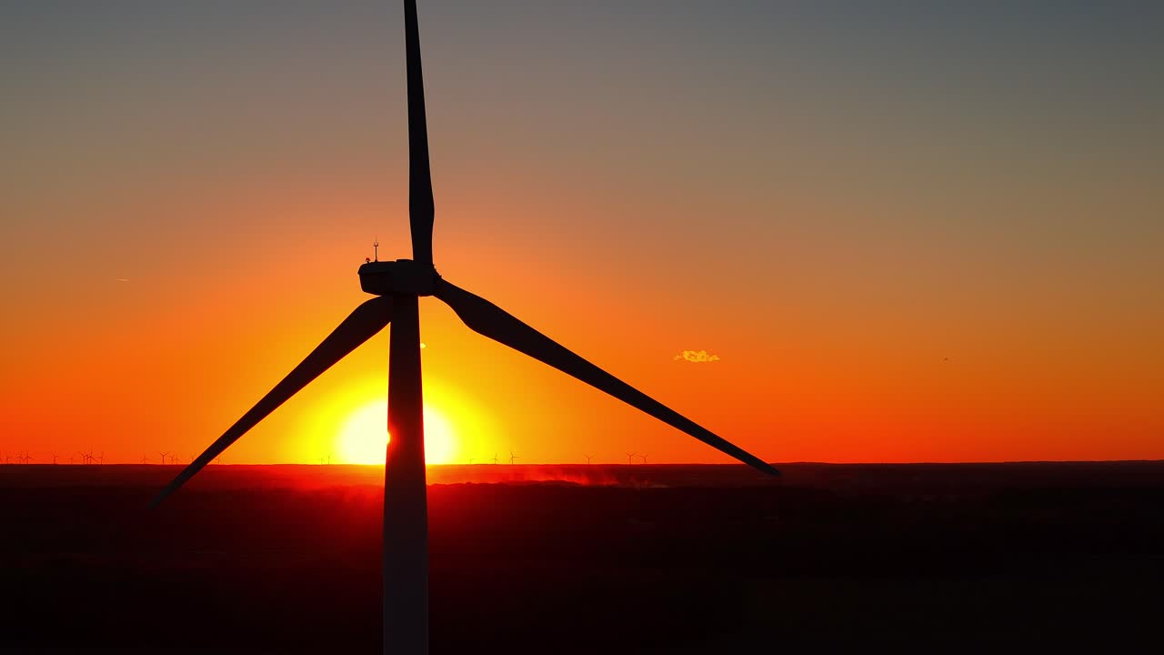 Rotor einer Windkraftanlage dreht sich, erzeugt erneuerbaren Strom, während die Sonne über dem Horizont untergeht, mit Textfreiraum auf der rechten Seite.