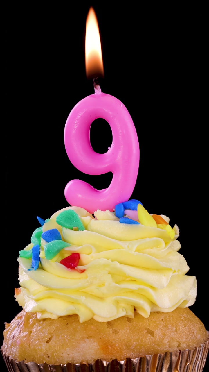 Una candela rosa numero nove su un cupcake decorato viene spenta, con il fumo che sale su uno sfondo nero sotto un'illuminazione brillante e uniforme e un'inquadratura statica