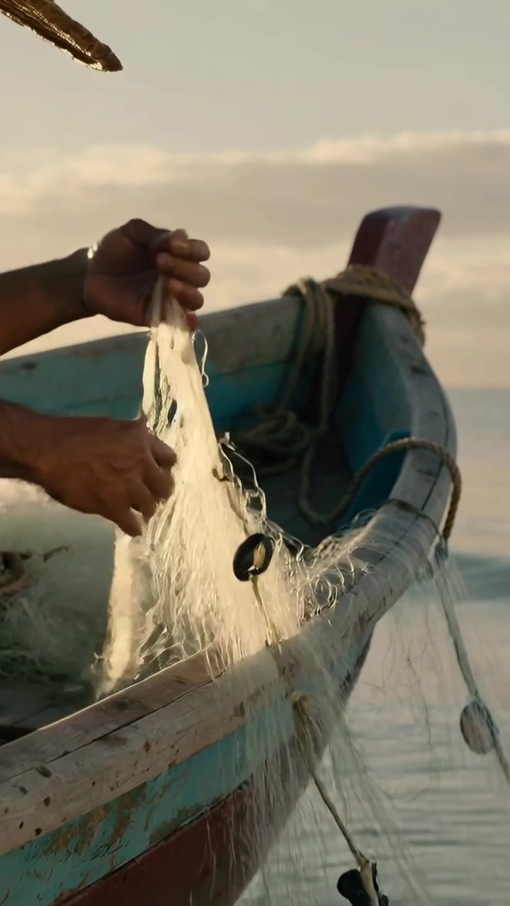 Video vertical: Manos de pescador levantando y tirando, extendiendo la red en una barca, preparándose para lanzar con flotador.