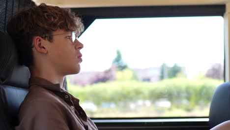 young boy sitting quietly on a bus, gazing out the window with a thoughtful expression