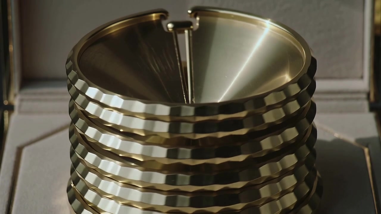 Camera revealing faceted cylinder with conical top on padded pad, metal arm engaging notch for view