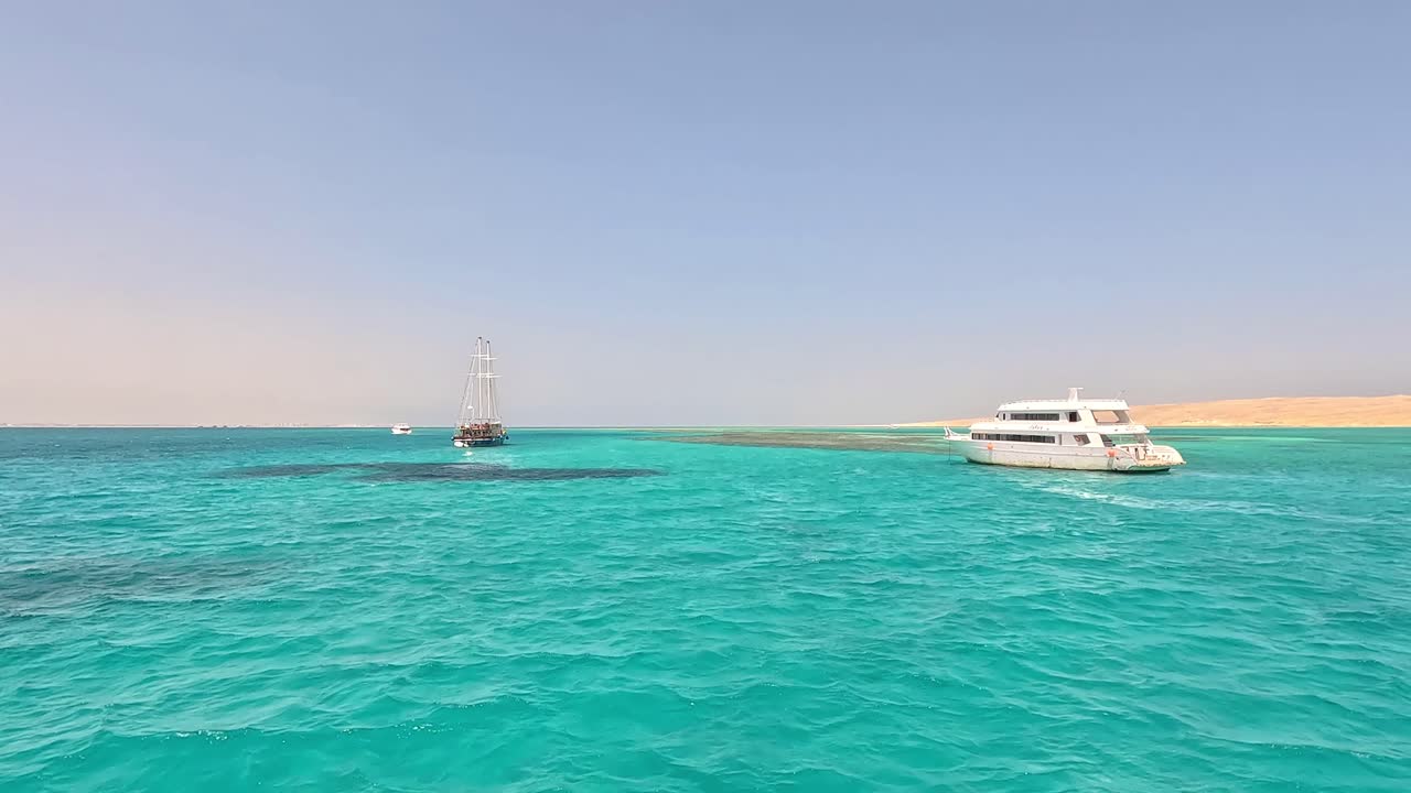 A frigate and a yacht in turquoise waters beyond the dunes of Egypt