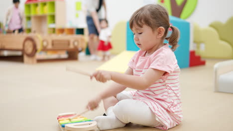 active toddler girl strikes fast on toy xylophone wooden keys in playroom kids cafe -profile view, slow motion