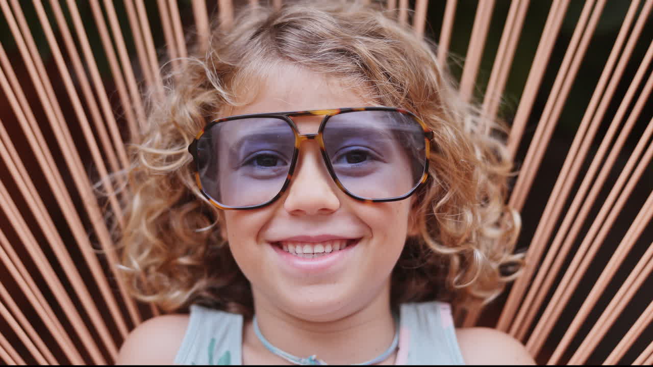 Cool little girl in a garden chair with sunglasses making faces