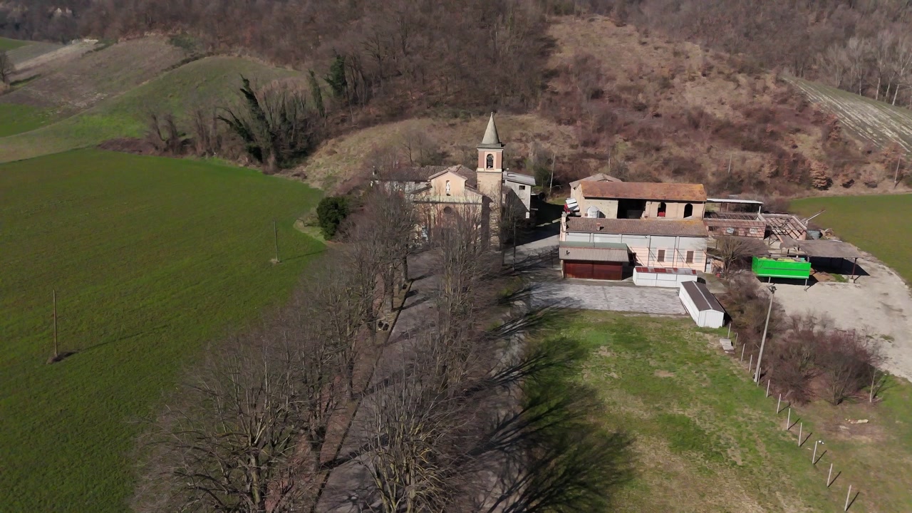 La chiesa di Sant'Ilario Vescovo domina Chiavenna Rocchetta, Lugagnano Val d'Arda, Piacenza, Emilia-Romagna, Italia, immersa tra boschi e terreni agricoli, ripresa con discesa del drone.