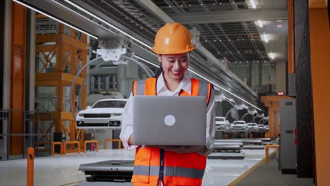 asian female engineer with safety helmet working on a laptop while standing in ev car factory