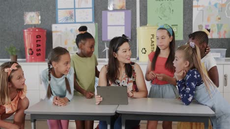 Happy-diverse-female-teacher-and-schoolgirls-using-tablet-in-elementary-school-class,-slow-motion