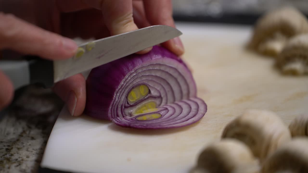 Handheld close up of hands cutting onion with paring knife in home kitchen